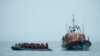 Migrantes são ajudados pela RNLI (Royal National Lifeboat Institution) antes de serem levados para a praia em Dungeness, costa sudeste da Inglaterra, Nov. 24, 2021, depois de atravessarem o Canal da Mancha.