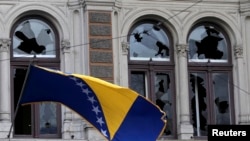 A Bosnian and Herzegovina national flag is seen on a damaged government building in Sarajevo February 8, 2014. Protesters across Bosnia set fire to government buildings and fought with riot police on Friday as long-simmering anger over lack of jobs and political inertia fuelled a third day of the worst civil unrest in Bosnia since a 1992-95 war. REUTERS/Antonio Bronic 
