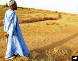 FILE - A farmer in Senegal walks across parched land which used to be a riverbed.