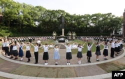 Siswa sekolah menengah mengelilingi monumen yang menandai hiposentrum bom atom dengan "rantai manusia" untuk menyerukan perdamaian dunia, di Nagasaki pada 9 Agustus 2024, pada peringatan 79 tahun bom atom di kota tersebut. (JIJI PRESS/AFP)