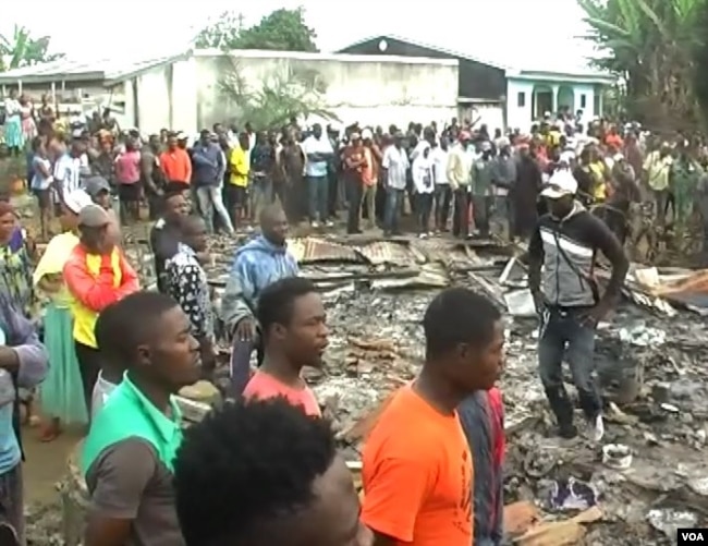 People are seen gathered at the remains of an inn burned down by an angry mob suspecting the inn's owner to be linked to child trafficking, in Kiossi, Cameroon, March 3, 2018. (M. Kindzeka/VOA)