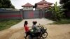 Women ride a motorcycle past a house in Phnom Penh, Cambodia, that is used to temporarily house asylum seekers sent from a Nauru detention center, Aug. 31, 2015.