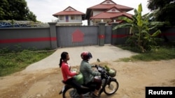 Women ride a motorcycle past a house in Phnom Penh, Cambodia, that is used to temporarily house asylum seekers sent from a Nauru detention center, Aug. 31, 2015.