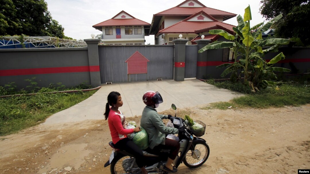 Women ride a motorcycle past a house in Phnom Penh, Cambodia, that is used to temporarily house asylum seekers sent from a Nauru detention center, Aug. 31, 2015.
