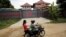 Women ride a motorcycle past a house in Phnom Penh, Cambodia, that is used to temporarily house asylum seekers sent from a Nauru detention center, Aug. 31, 2015.