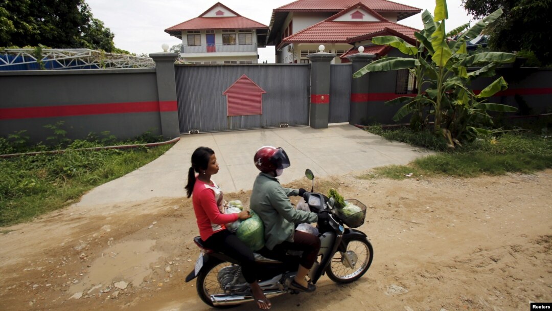 Phụ nữ lái xe máy qua một ngôi nhà tại Phnom Penh, Campuchia, được sử dụng để tạm giam người tị nạn được gửi đến từ trung tâm giam giữ Nauru.