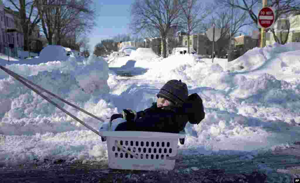 Eli Bokor rides in a laundry basket down a snow-covered street in southeast Washington, Jan. 24, 2016. His father, not seen in the photo, is pulling the basket.