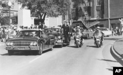 FILE - Seen through the limousine's windshield as it proceeds along Elm Street past the Texas School Book Depository, President John F. Kennedy appears to raise his hand toward his head within seconds of being fatally shot in Dallas, Nov 22, 1963.