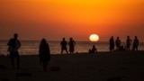 In this file photo, people watch a sunset sitting on a beach next to the Trafalgar Lighthouse in Los Caños de Meca, Spain, on, July 29, 2020. (AP Photo/Emilio Morenatti, File)