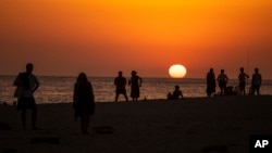 In this file photo, people watch a sunset sitting on a beach next to the Trafalgar Lighthouse in Los Caños de Meca, Spain, on, July 29, 2020. (AP Photo/Emilio Morenatti, File)