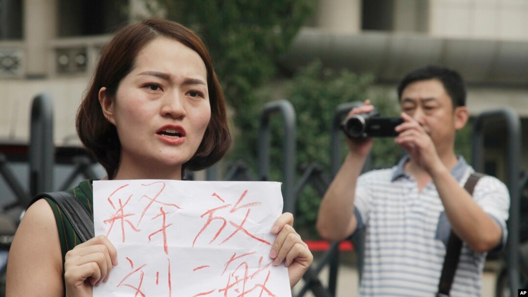 FILE - In this Aug. 1, 2016 file photo, a man films Li Wenzu, left, wife of imprisoned lawyer Wang Quanzhang, holds a paper that reads "Release Liu Ermin" as she and supporters of a prominent Chinese human rights lawyer and activists stage a protest outside the Tianjin No. 2 Intermediate People's Court in Tianjin, China. 