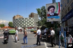 Pedestrians walk under an electoral banner of presidential candidate Ebraim Raisi in a square in downtown Tehran, Iran, Thursday, May 11, 2017.