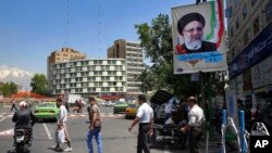 Pedestrians walk under an electoral banner of presidential candidate Ebraim Raisi in a square in downtown Tehran, Iran, Thursday, May 11, 2017.