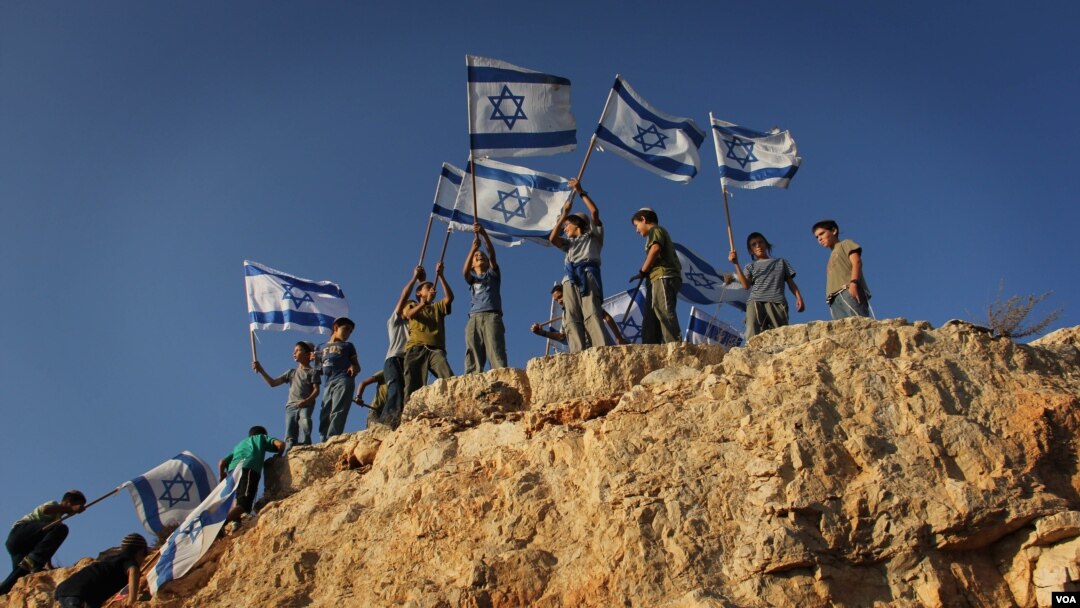 Children in the West Bank settlement of Itamar wave Israeli flags on a hilltop. (file) (VOA/Rebecca Collard)