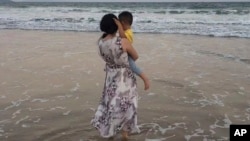 In this photo released by Zou Xiaoqi, Zou Xiaoqi, a single mother turned activist in Shanghai, holds her son as they visit a beach in Sanya, southern China's Hainan province in October, 2019. 