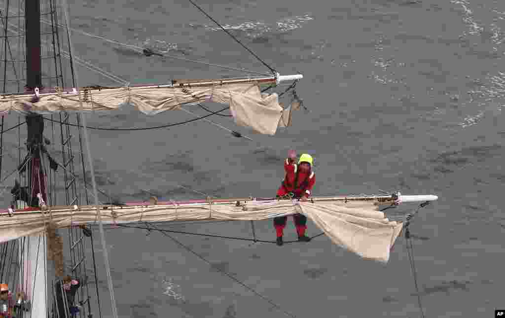 Seorang pelaut di atas tiang kapal melambaikan tangannya saat menurunkan layar (3/10). (AP/Rob Griffith) 