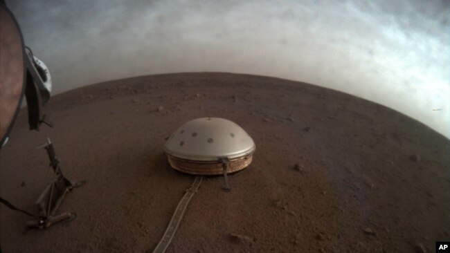 In this undated photo made available by NASA on Thursday, July 22, 2021, clouds drift over the dome-covered SEIS seismometer of the InSight lander on the surface of Mars.