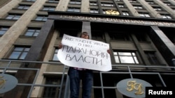 FILE - A lone activist protests against a restrictive law targeting foreign-funded NGOs working in Russia, outside a government building in Moscow, July 6, 2012. His placard reads "Tightening the law concerning NGOs [attests to] the paranoia of the authorities."