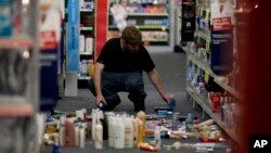 Seorang pria memunguti barang-barang yang berjatuhan akibat gempa di sebuah toko di di La Mirada, California (28/3). (AP/Jae C. Hong)