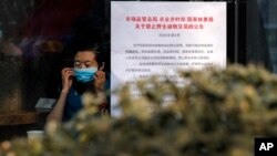 A woman puts on a mask near a notice board that reads "Bans on wild animals trading following the coronavirus outbreak" at a cafe in Beijing, Monday, Feb. 10, 2020.