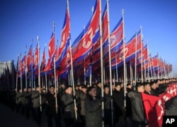 ຊາວເກົາຫລີເໜືອ ເດີນສວນສະໜາມ ຖືທຸງເກົາຫລີເໜືອ ຢູ່ຈະຕຸລັດ Kim Il Sung.