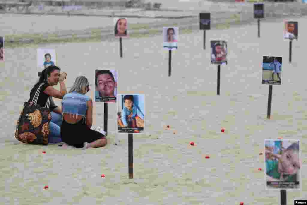 Vanessa Freitas Moreira sits next to the photo of her son Joao Vitor Moreira dos Santos, in a demonstration of NGO Rio de Paz displaying pictures of children who were shot dead during police operations during the administration of Rio de Janeiro&#39;s governor Claudio Castro, at Copacabana beach in Rio de Janeiro, Brazil.