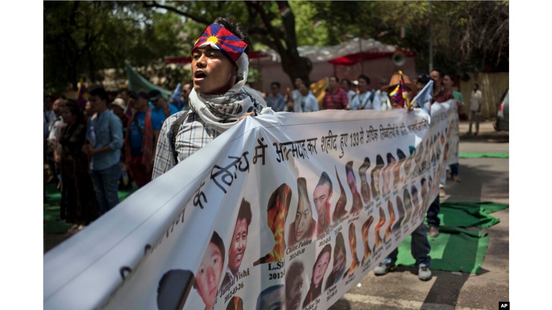 FILE - A Tibetan exile sings the national anthem as he holds a banner with others showing the portraits of Tibetan self-immolators during a protest in New Delhi, April 25, 2014.