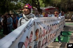 FILE - A Tibetan exile sings the national anthem as he holds a banner with others showing the portraits of Tibetan self-immolators during a protest in New Delhi, April 25, 2014.