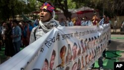 FILE - A Tibetan exile sings the national anthem as he holds a banner with others showing the portraits of Tibetan self-immolators during a protest in New Delhi, April 25, 2014.