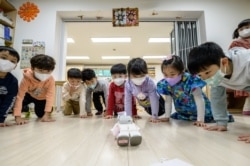 Anak-anak melakukan push up bersama robot "Alpha Mini" setinggi 24,5 sentimeter (9,6 inci), 23 November 2021,