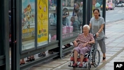 FILE - Caregiver pushes elderly wheelchair-bound woman through Taipei, Taiwan, Sept. 30, 2013.