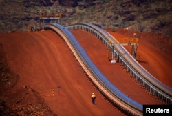 FILE - A worker walks near conveyer belts loaded with iron ore at the Fortescue Solomon iron ore mine located in the Valley of the Kings, around 400 km (248 miles) south of Port Hedland in the Pilbara region of Western Australia.