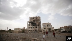 也门萨那居民站在一座被沙特领导的联军空袭炸毁的房屋前. (2015年7月6日)