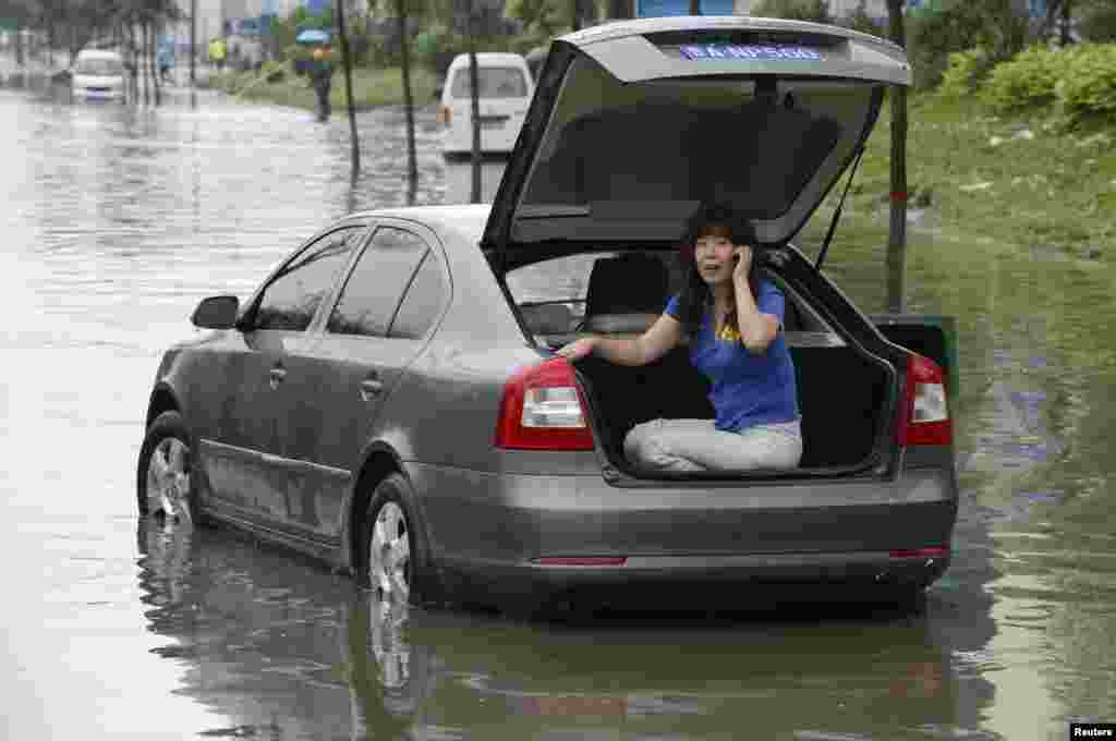 A woman talks on her mobile phone at the trunk of her car as she waits for rescue on a flooded street in Taiyuan, Shanxi province, China, July 31, 2012.