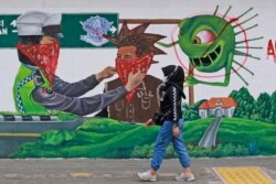 Seorang perempuan berjalan melewati mural bertema virus corona yang menyerukan agar masyarakat selalu menggunakan masker untuk menekan penyebaran COVID-19, di Medan, Sumatera Utara, Indonesia, Senin 1 November 2021. (Foto: AP)