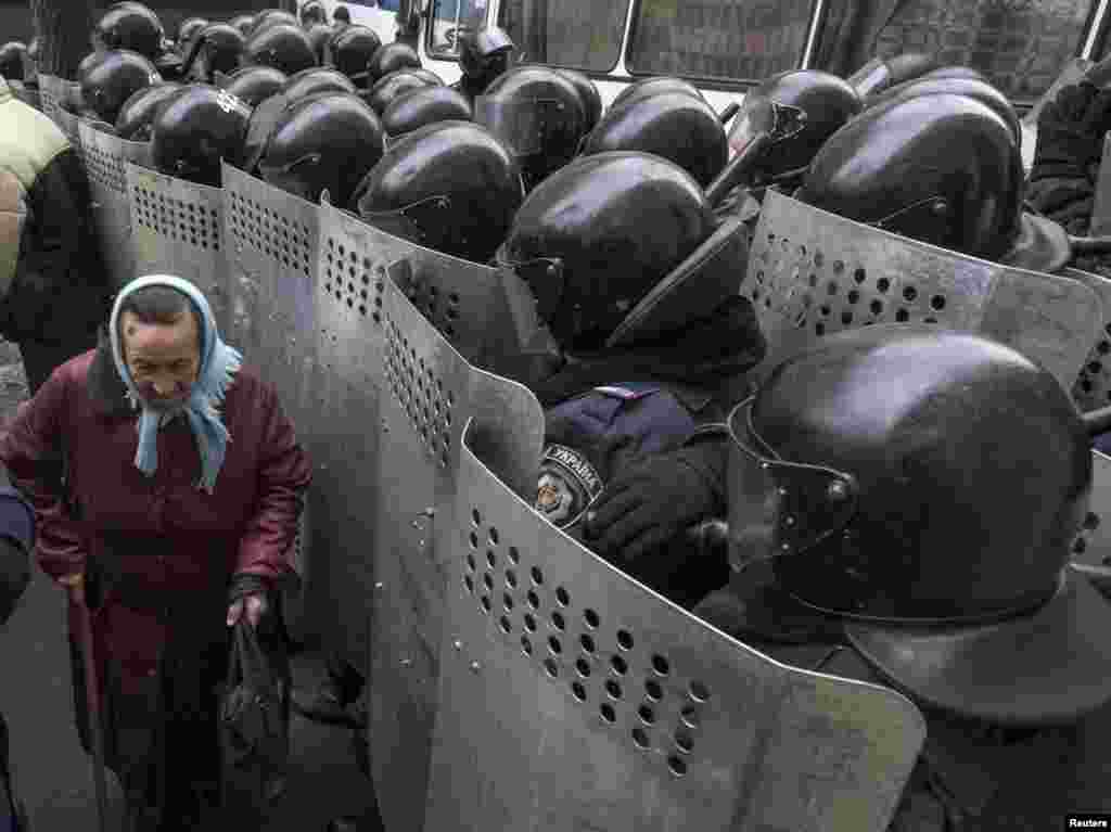 A woman passes by Interior Ministry personnel as they block pro-EU demonstrators near the Ukrainian Ministry of Internal Affairs in Kyiv, Ukraine, Dec. 20, 2013. 