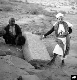 FILE - Two Yemenis stand near a column bearing ancient South Arabian script at the Awwam Temple, also known as the Mahram Bilqis in Marib, Yemen, in February 1957.