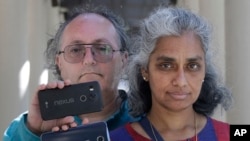 In this July 25, 2018 photo, Kalyanaraman Shankari, right, and her husband Thomas Raffill hold their phones while posing for photos in Mountain View, Calif. (AP Photo/Jeff Chiu)