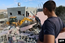 Warga Palestina menyaksikan sebuah ekskavator menyapu puing-puing rumah wakil kepala biro politik Hamas Saleh al-Aruri setelah rumah itu dihancurkan oleh pasukan Israel di Tepi Barat yang diduduki pada 31 Oktober 2023. (Foto: AFP)