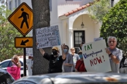 Protesters wave signs at Florida Gov. Ron DeSantis as he and Vice President Mike Pence visit Westminster Baldwin Park, May 20, 2020, in Orlando, Fla.