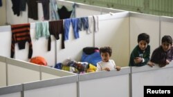 FILE - Children watch as they stand on beds in a shelter for migrants inside a hangar of the former Tempelhof airport in Berlin, Germany, Dec. 9, 2015. 