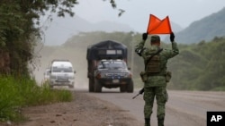 FILE - A soldier wearing an armband for Mexico's National Guard signals for vehicles to stop at a temporary checkpoint to look for migrants in northbound vans and trucks, just north of Ciudad Cuauhtemoc, Chiapas State, Mexico, June 15, 2019. 