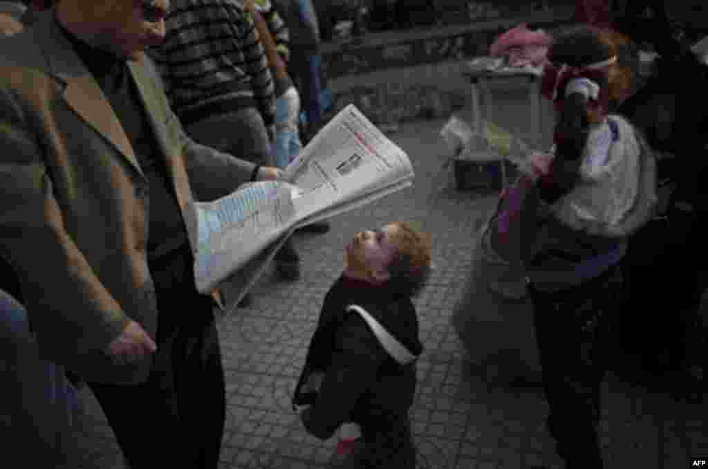 A boy looks at a newspaper in Tahrir Square, Cairo, Egypt, Wednesday, Feb. 9, 2011. Protesters appear to have settled in for a long standoff, turning Tahrir Square into a makeshift village with tens of thousands coming every day, with some sleeping in ten