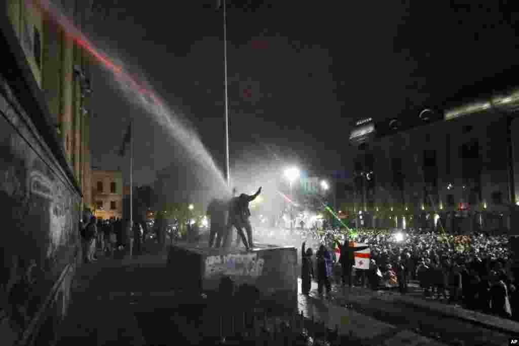 Demonstrators stand atop of a tomb under running water from a water cannon rallying outside the parliament&#39;s building to continue protests against the government&#39;s decision to suspend negotiations on joining the EU in Tbilisi, Georgia.