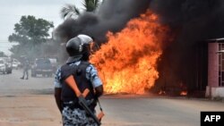 An Ivorian police officer stands near a burning bus in Abidjan, Sept. 10, 2015. Clashes broke out in several Ivorian cities after people tried to protest following the release of the names of candidates for October presidential elections.