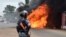 An Ivorian police officer stands near a burning bus in Abidjan, Sept. 10, 2015. Clashes broke out in several Ivorian cities after people tried to protest following the release of the names of candidates for October presidential elections.