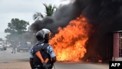 Un officier de police ivoirien se tient près d'un bus en feu à Abidjan, le 10 septembre 2015.