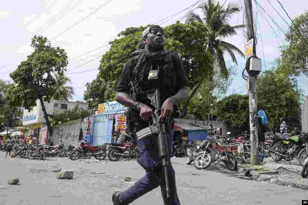 A police officer advances with his weapon toward a gas station to disperse a crowd threatening to burn down the gas station because they believed the station was withholding gas, in Port-au-Prince, Haiti, Oct. 23, 2021.