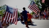 A boy carries American flags through Barnstable Village, Massachusetts, on Cape Cod during the annual Fourth of July Parade celebrating the country's Independence Day on July 4, 2024.