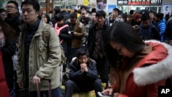 A man, center, sits on his belongings as he waits with other Chinese travelers to board at the south train station in Beijing, Jan. 31, 2016. 